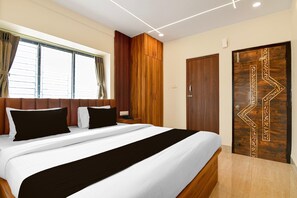 A hotel room with a large bed, a wooden wardrobe, a door with intricate carvings, and a window with curtains. - Classic Newtown Bus Stand (Barasat)