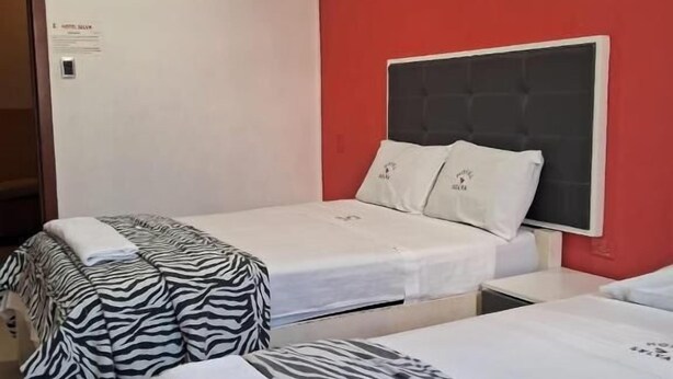 Habitación de hotel con dos camas, cada una con una colcha de estampado de cebra, una pared de acento roja y un techo blanco.