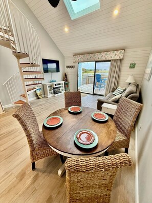 A dining area with a round table, wicker chairs, and a view of the outdoors. - Seas the Day Beach Retreat - Waterfront Views + Hot Tub + Kayaks (North Topsail Beach)