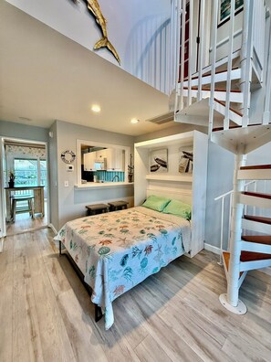 Ein Schlafzimmer mit Bett, Treppe, einer Küchenzeile und Blick ins Freie.