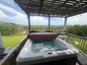 A hot tub under a wooden pergola with a view of a grassy field and distant buildings. - Seas the Day Beach Retreat - Waterfront Views + Hot Tub + Kayaks (North Topsail Beach)