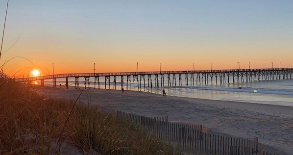 A pier extending over a beach with the sun setting in the background. - Seas the Day Beach Retreat - Waterfront Views + Hot Tub + Kayaks (North Topsail Beach)