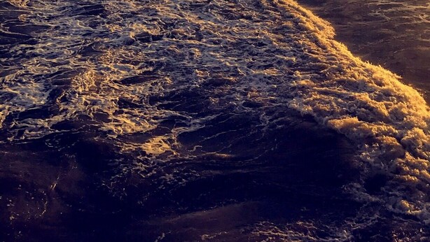 Una playa con olas, un atardecer y edificios al fondo.