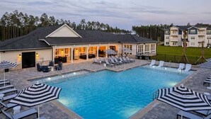 Piscina com espreguiçadeiras e guarda-sóis, um terraço coberto e um edifício com telhado inclinado.