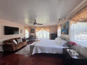 Ein Schlafzimmer mit Bett, Schreibtisch, Stuhl, Fernseher und Deckenventilator.