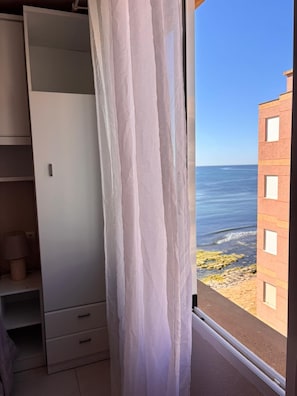 Una habitación con vista al mar, un armario blanco y una ventana con cortina.