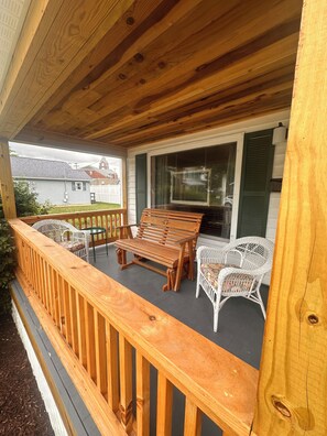 Eine Holzterrasse mit einer Bank und Stühlen, einem überdachten Bereich und Blick auf ein Haus im Hintergrund.