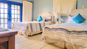 A hotel room with two beds, a nightstand, a lamp, and a view through a blue door. - Chic casual ocean themed condo located  in Tobago 's most exclusive compound . (Lowlands)