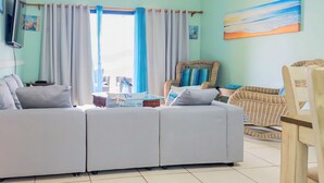 A living room with a sectional sofa, a round coffee table, and a chair. - Chic casual ocean themed condo located  in Tobago 's most exclusive compound . (Lowlands)