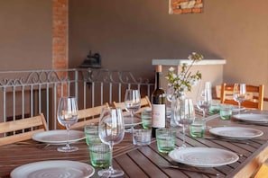 A wooden dining table set with plates, wine glasses, and a bottle of wine. - Casa delle Noci - Five Bedroom Villa, Sleeps 15 (Villafranca d'Asti)