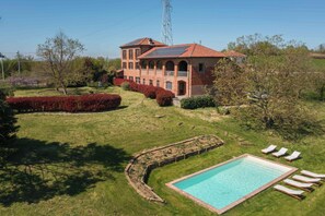 A large house with a swimming pool, surrounded by a well-maintained lawn and garden.