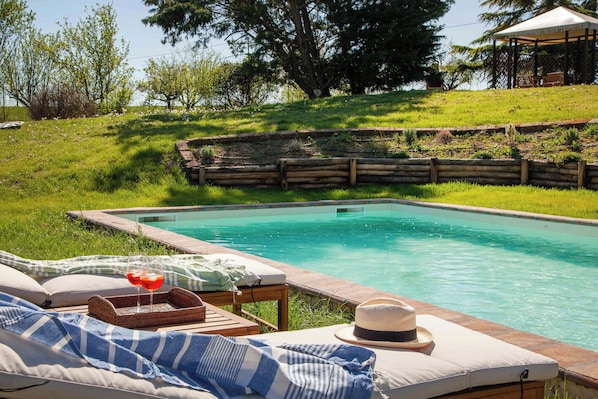Un espace aménagé au bord de la piscine, avec un fauteuil de relaxation, un chapeau et un plateau avec des boissons.