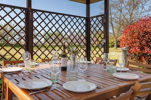 Une table en bois, dressée pour le repas, avec des assiettes, des couverts et des verres à vin, une bouteille de vin et un vase rempli de fleurs.