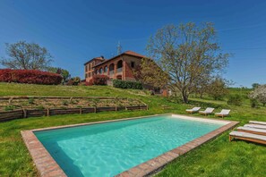 A rectangular swimming pool with a brick border, surrounded by grass and a wooden fence.