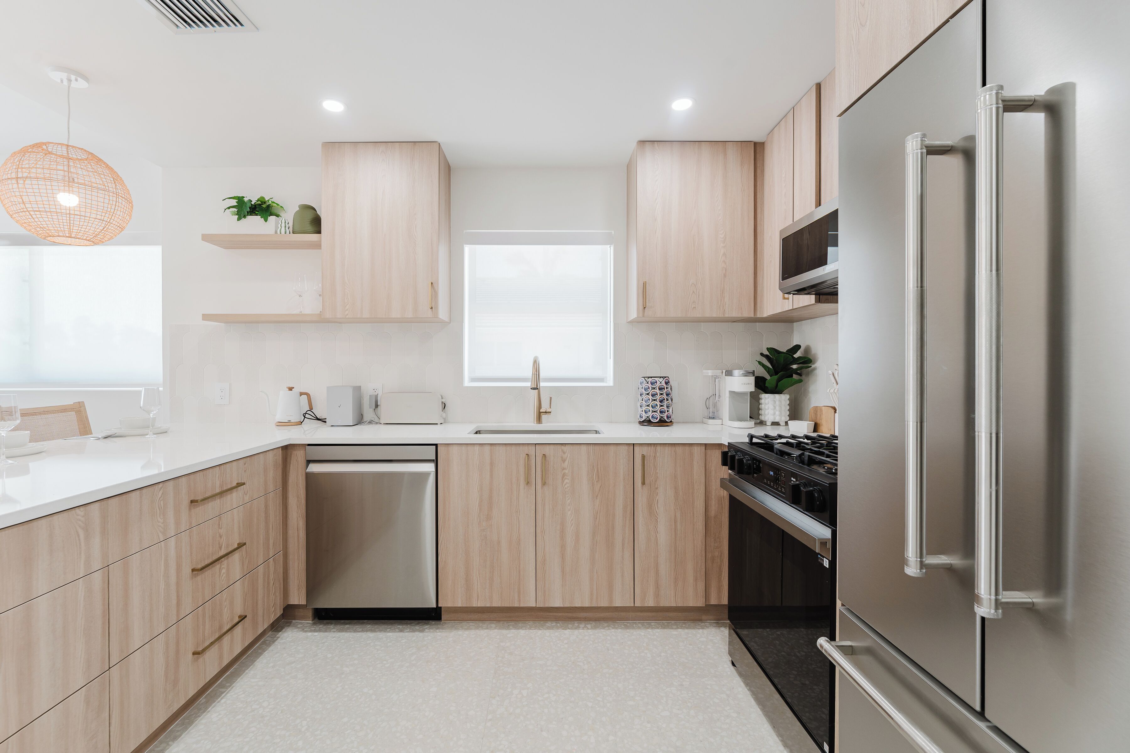 Una cocina moderna con armarios de madera clara, electrodomésticos de acero inoxidable y encimera blanca.