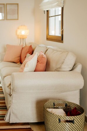 Ein beiges Sofa mit Kissen, einer Lampe, einem Fenster und einem gewebten Korb.