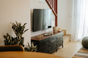 Ein modernes Wohnzimmer mit einem an der Wand befestigten Flachbildfernseher, einem Holzkonsolentisch mit Dekoration und einer Treppe, sowie einem Blumentopf.