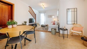 Un salon moderne comprenant une table à manger, des chaises, un canapé, un téléviseur, un escalier et une grande fenêtre.