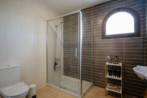 Une salle de bain avec une douche à parois de verre, des toilettes, un lavabo et une étagère contenant des articles de toilette.