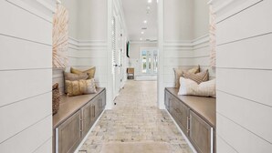A hallway with a brick floor, white walls, and a view into a room with a door. - NEW Laguna Serenity | 7BR Gulf Front | Pool | LSV/Bikes (Panama City Beach)