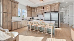 A modern kitchen with wooden cabinets, a central island with bar stools, stainless steel appliances, and a pendant light. - NEW Laguna Serenity | 7BR Gulf Front | Pool | LSV/Bikes (Panama City Beach)