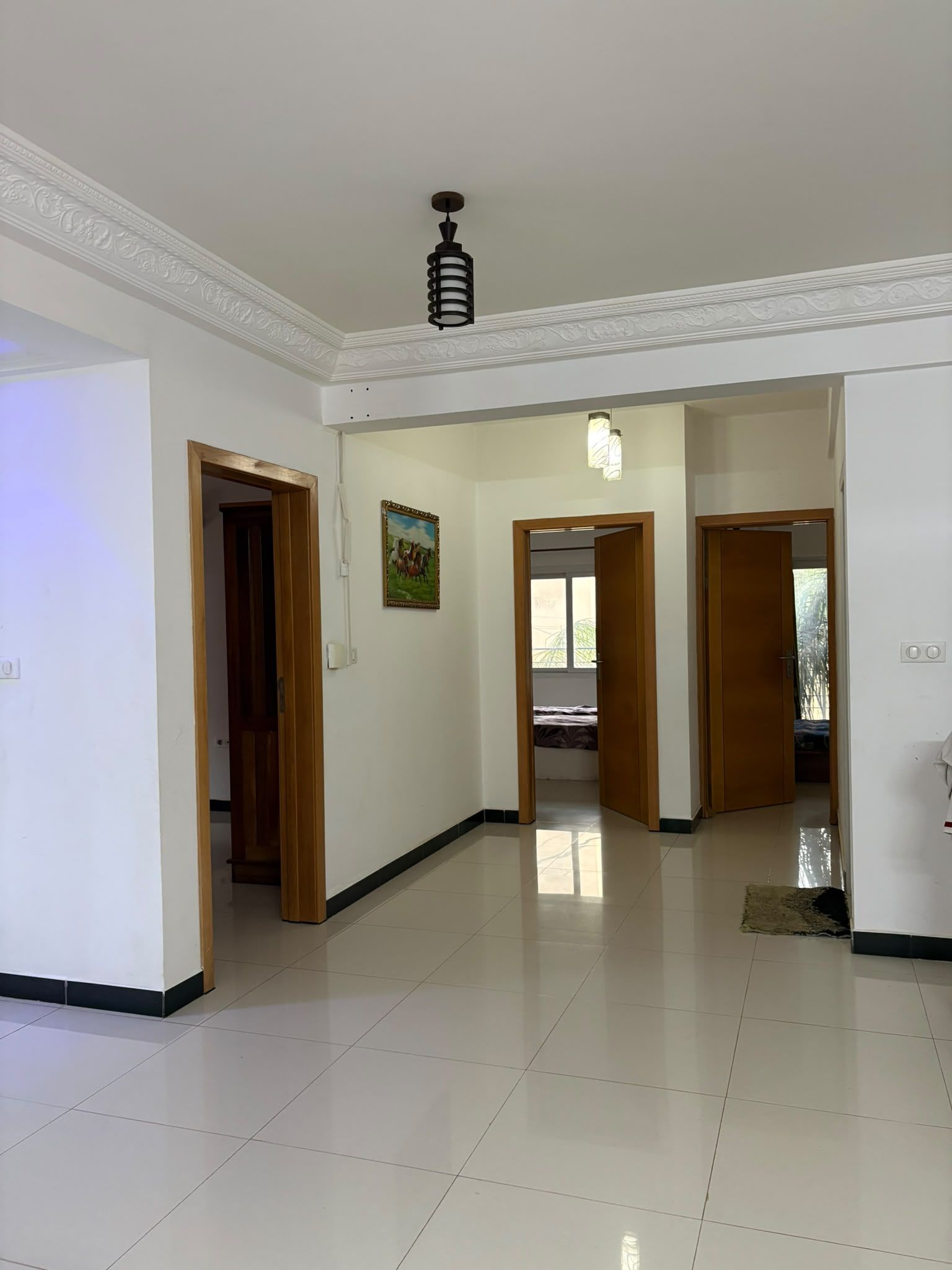 A spacious hallway with white walls, a tiled floor, and multiple doorways leading to other rooms.