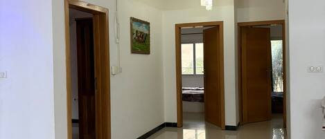A spacious hallway with white walls, a tiled floor, and multiple doorways leading to other rooms.