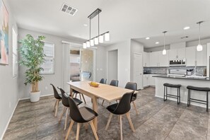 Eine moderne Küche mit weißen Schränken, einer Mikrowelle und einem Spülbecken. Es gibt einen Essbereich mit einem Holztisch und schwarzen Stühlen.