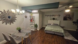 Une pièce de taille modeste comprenant une table à manger, des chaises, un lit, un ventilateur de plafond et un climatiseur fixé au mur.
