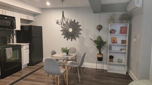Une cuisine moderne avec des meubles blancs, un réfrigérateur noir et un coin repas comprenant une table en verre et des chaises grises.