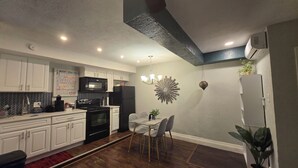 Une cuisine moderne avec des meubles blancs, un micro-ondes noir et un coin repas comprenant une table et des chaises en verre.