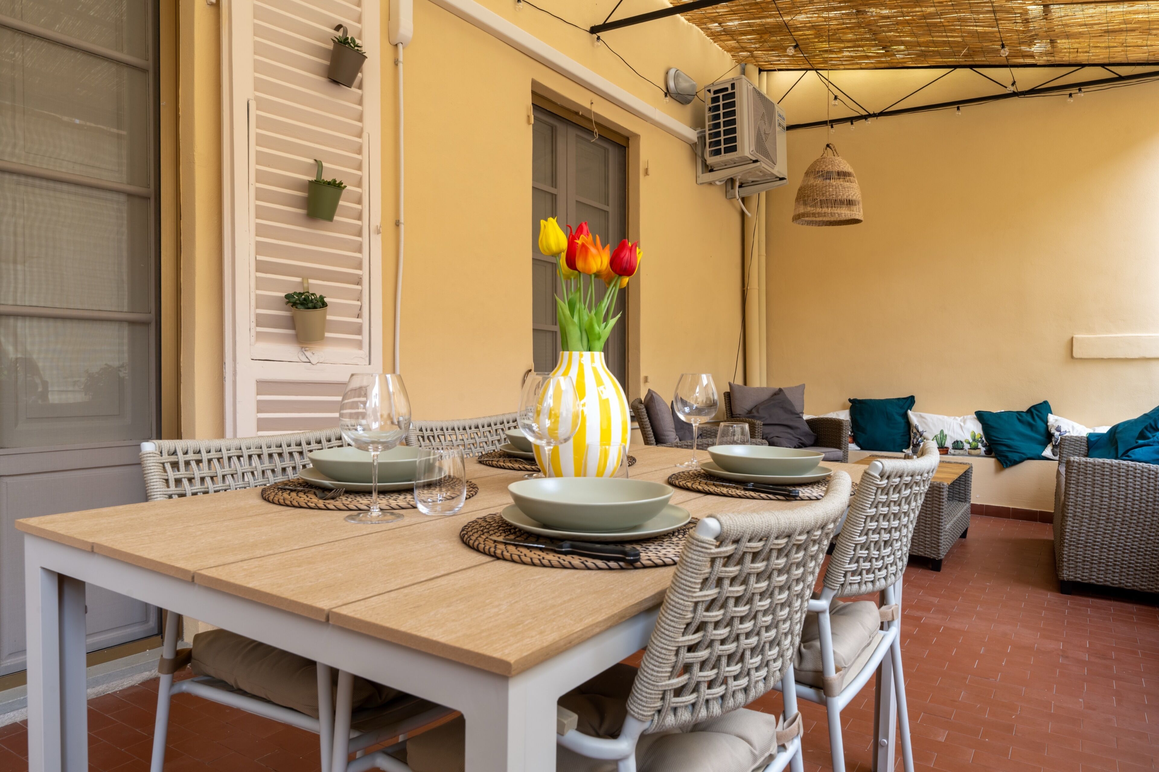 Un coin repas avec une table dressée pour quatre personnes, des chaises en osier et un vase rempli de fleurs.
