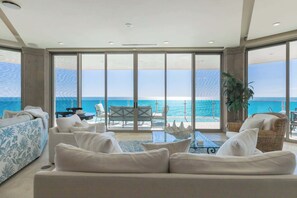 Ein modernes Wohnzimmer mit einer großen Couch, einem Esstisch und Stühlen, mit Blick auf einen Balkon und das Meer.