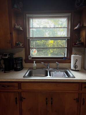 A kitchen with a double sink, a coffee maker, a bottle of dish soap, and a window with blinds.