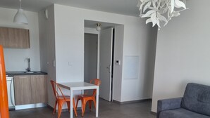 Una sala moderna con un sofá gris, una mesa de centro blanca y un comedor con sillas naranjas.