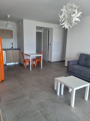 Ein modernes Wohnzimmer mit grauem Sofa, einem weißen Couchtisch und einem Essbereich mit orangefarbenen Stühlen.