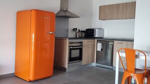 Una cocina moderna con un refrigerador naranja grande, un microondas, una estufa y un comedor con una silla.