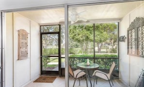 Une pièce dotée d’une porte-fenêtre coulissante donnant sur un balcon équipé d’une table et de chaises, ainsi que d’un ventilateur de plafond et d’un élément décoratif mural.