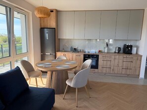 A modern kitchen with a dining area, wooden cabinets, a refrigerator, and a coffee machine.