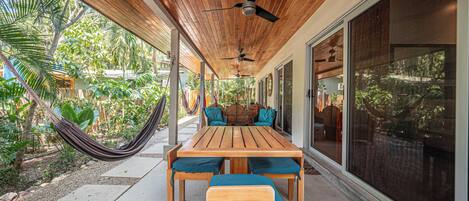 Une terrasse couverte avec une table et des chaises en bois, un hamac et de grandes portes-fenêtres coulissantes.