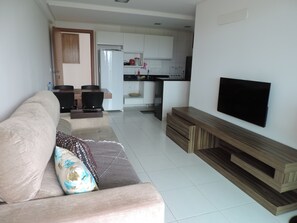 Ein Wohnzimmer mit einer Couch, einem Fernseher und einer Küche im Hintergrund.