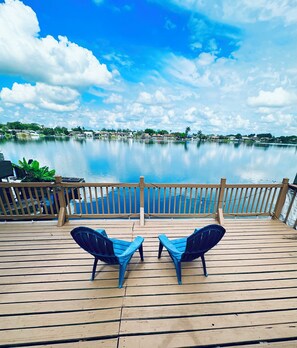 A wooden deck with two blue chairs facing a calm lake, surrounded by a wooden fence. - Lake Villas Miami . Breathtaking View . Prime location (Fort Lauderdale)
