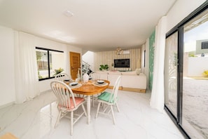 A dining area with a wooden table and white chairs, a sofa, and a TV in the background. - Villa for 7 people with private Picuzzi in Punta Cana. Close to everything! (Punta Cana)
