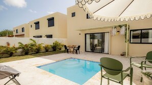A swimming pool with a tiled edge, surrounded by outdoor furniture, and a building with a covered patio area. - Villa for 7 people with private Picuzzi in Punta Cana. Close to everything! (Punta Cana)