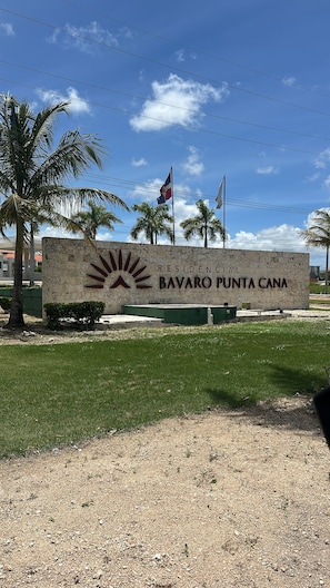 Une enseigne indiquant « Residencia Bavaro Punta Cana », avec des palmiers et des drapeaux en arrière-plan.