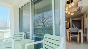 Ein Balkon mit Glastür, eine Essecke mit Holzmöbeln und Blick auf Bäume.