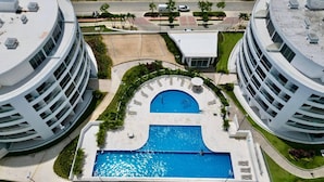 Ein modernes Gebäude mit einem zentral gelegenen Schwimmbad, umgeben von Grünflächen und angrenzend zu ähnlichen Bauwerken.