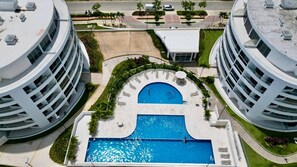 A modern building with a central swimming pool, surrounded by greenery and adjacent to other similar structures. - Luxury Family Retreat , Private Beach & Pool (Cartagena)