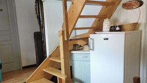Een houten trap die leidt naar een vide, een witte koelkast en een houten eettafel met stoelen.