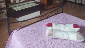 Een kamer met een bed, een houten garderobe, een wandklok en een klein tafeltje met boeken.